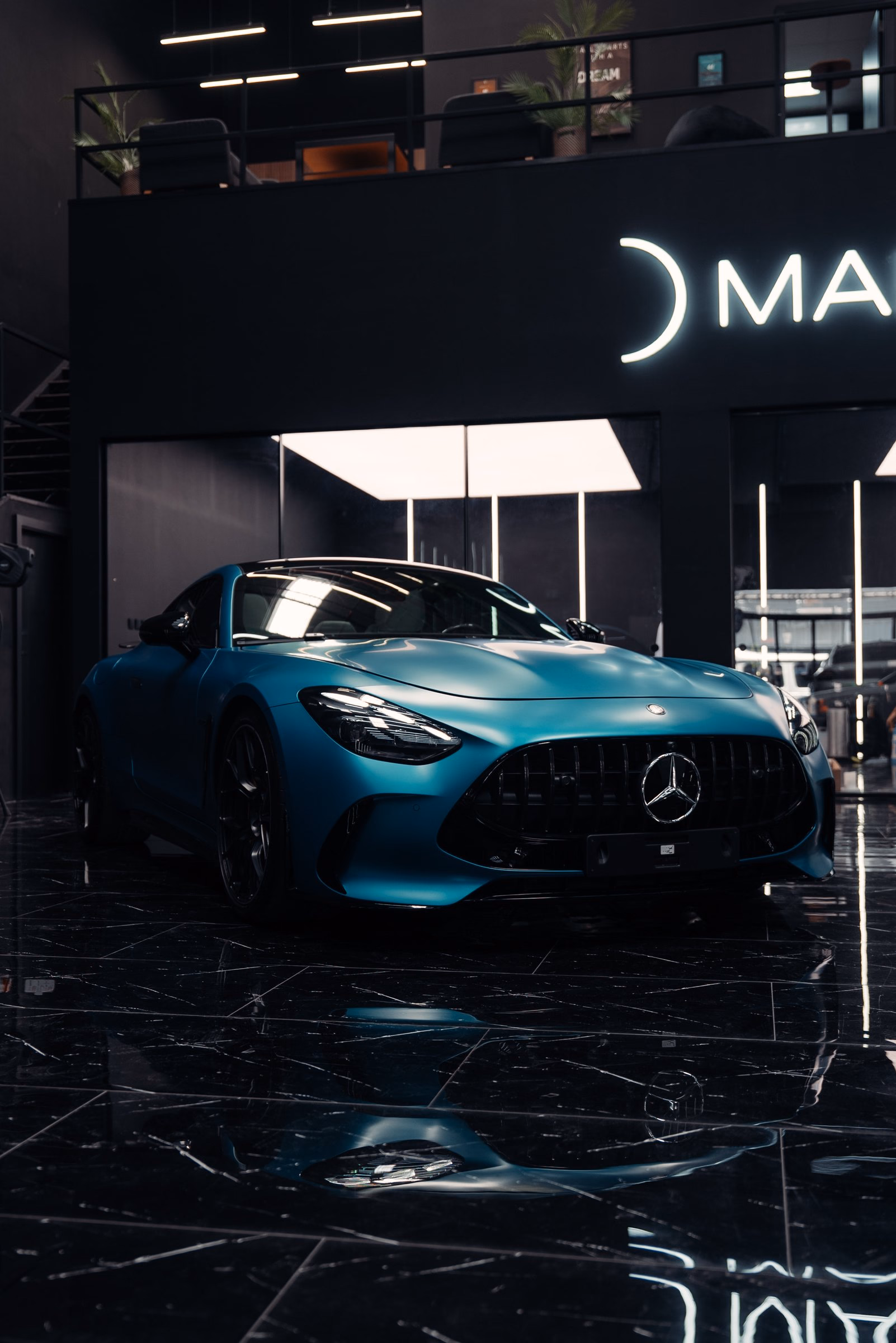 A satin teal Mercedes-AMG GT beneath the illuminated MAER sign after full body paint protection film