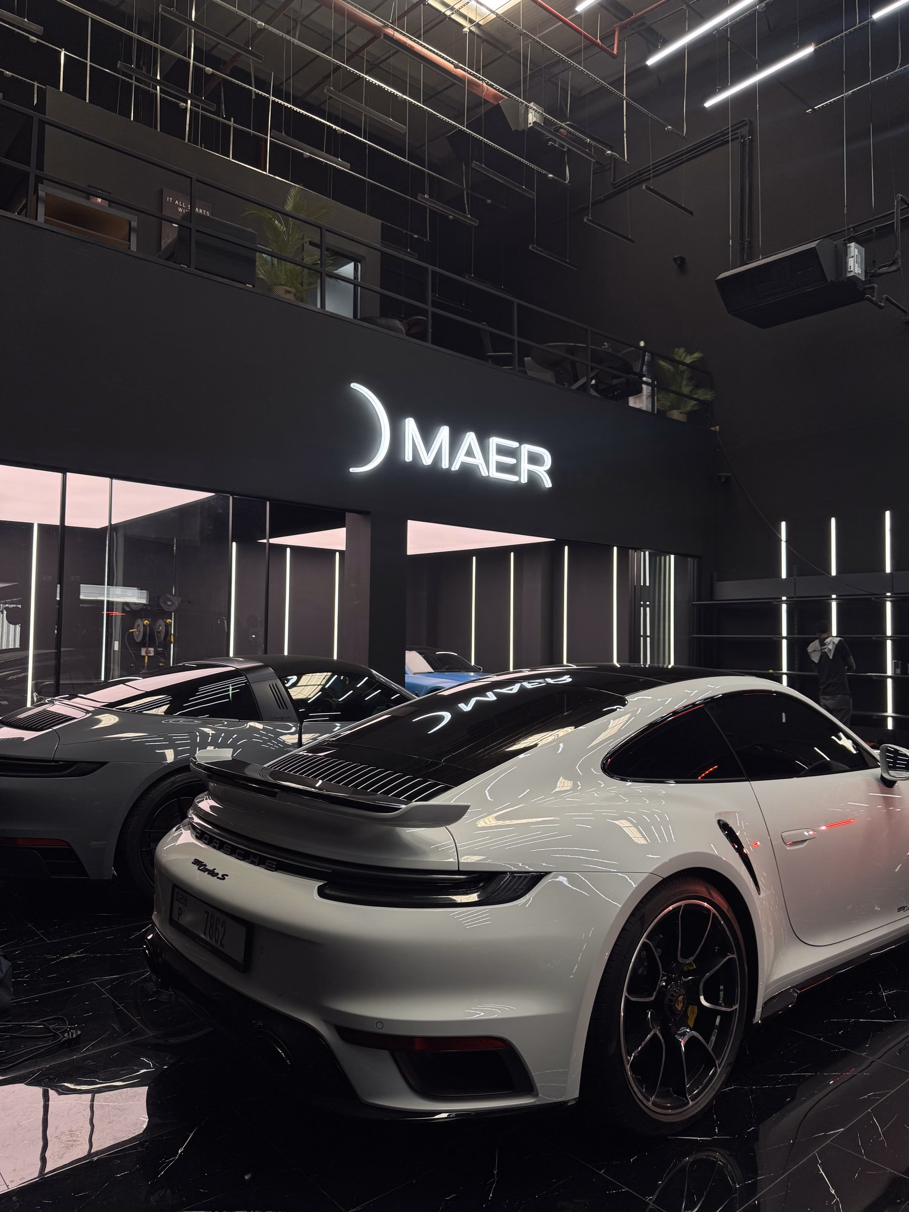 Two Porsche 911s photographed from the rear beneath the illuminated MAER sign after full body paint protection film