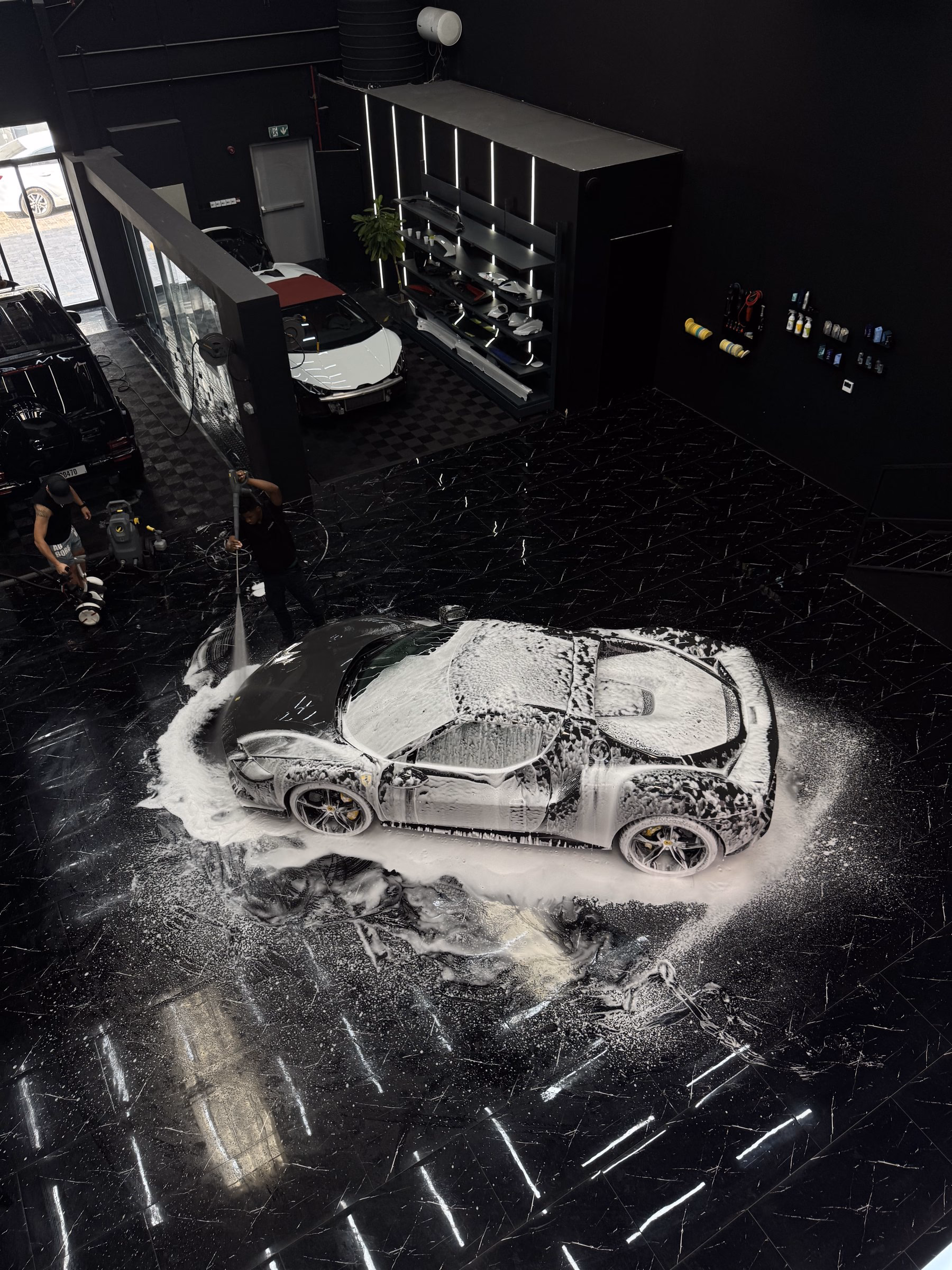 A Ferrari covered in cleaning foam under studio lighting at the MAER workshop in Al Quoz